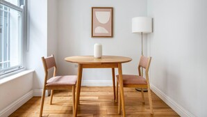 Um quarto com uma mesa redonda de madeira, duas cadeiras, um vaso branco, um abajur e uma obra de arte abstrata emoldurada na parede.