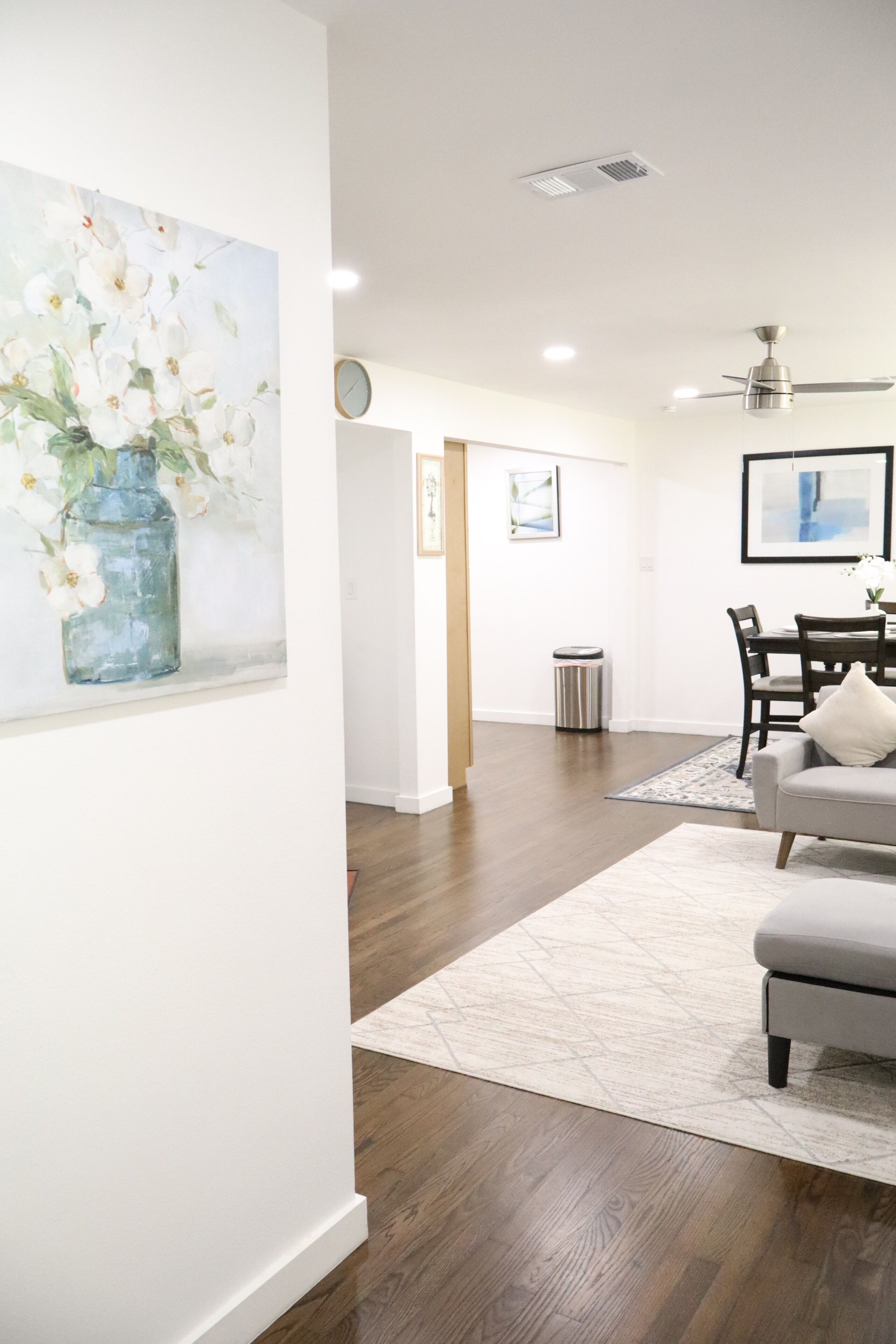 Een modern interieur met een eethoek, een woonkamer met een grijze bank en een hal met kunstwerken aan de wanden.