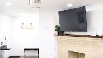 A modern living room with a fireplace, a flat-screen TV mounted above it, a ceiling fan, and a seating area with a sofa and a coffee table.