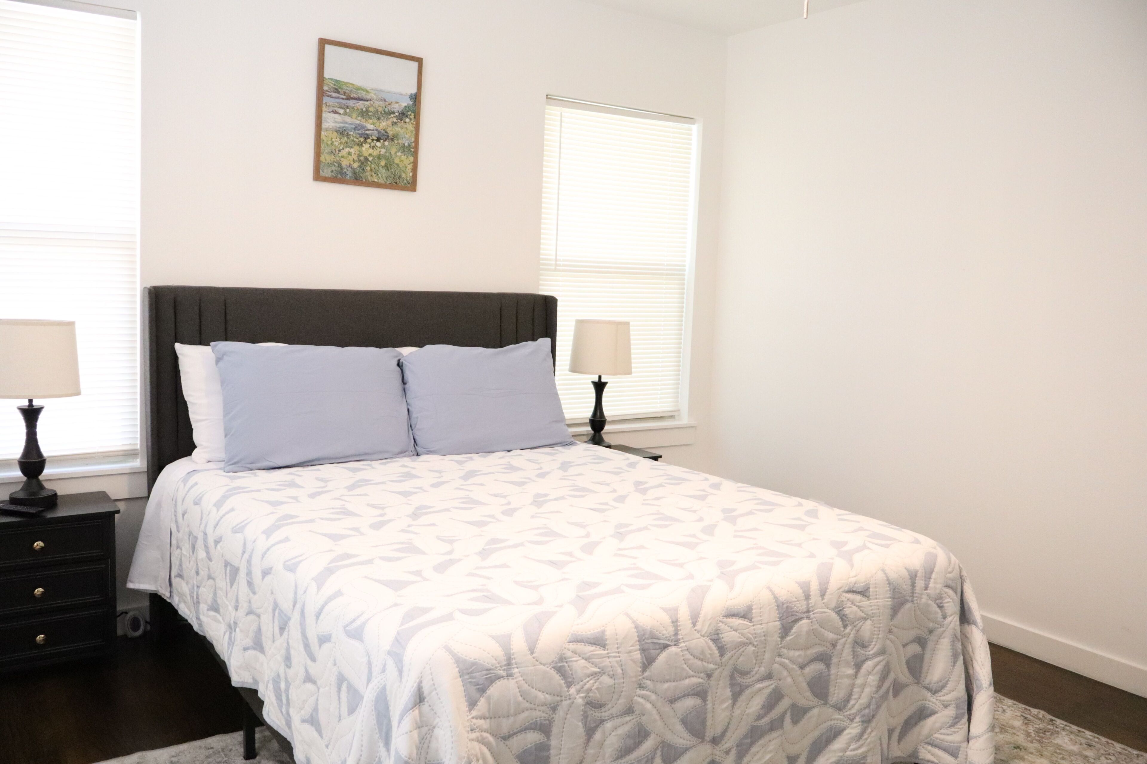 A bedroom with a bed, two bedside tables, a nightstand, a lamp, and a painting on the wall.