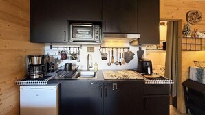 Eine kompakte Küche mit integriertem Mikrowellenherd, Kaffeemaschine und einem kleinen Kühlschrank.