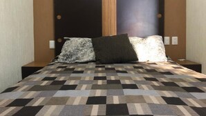 En säng med ett geometriskt mönstrat överkast, en sänggavel med cirkelformade utskärningar och två sänglampor.