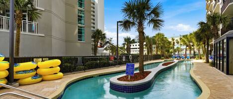 A swimming pool with a blue tiled edge, surrounded by palm trees and a brick walkway.