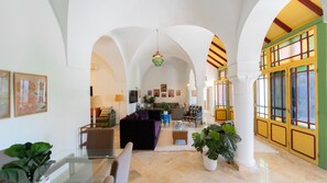 Ein Innenraum mit Gewölbedecken, einer Sitzecke mit Sofas, einem Couchtisch und Topfpflanzen.