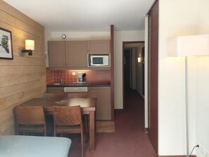 A compact kitchen with wooden cabinets, a microwave, a coffee maker, and a dining area with a table and chairs. - 100m from resort center, 8th floor, view forest, balcony, tv, ski locker, 27m², Les Arcs (Bourg-Saint-Maurice)