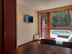 A room with a TV, a table, a sofa, and a window with a view of trees. - 100m from resort center, 8th floor, view forest, balcony, tv, ski locker, 27m², Les Arcs (Bourg-Saint-Maurice)