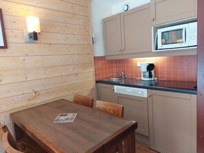 A compact kitchen with wooden walls, a dining table, and a microwave. - 100m from resort center, 8th floor, view forest, balcony, tv, ski locker, 27m², Les Arcs (Bourg-Saint-Maurice)
