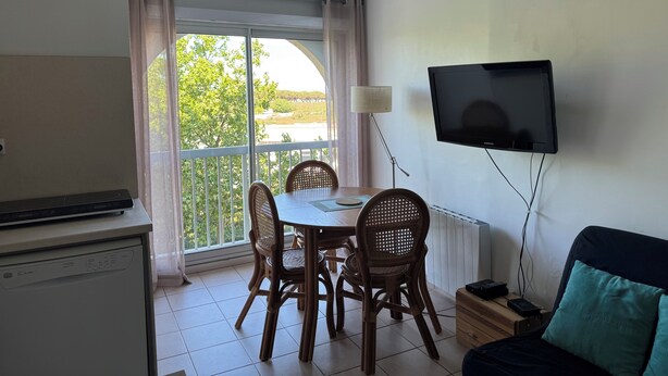 Een kamer met een eettafel, stoelen, een aan de muur bevestigde televisie, een bank en een raam met gordijnen.
