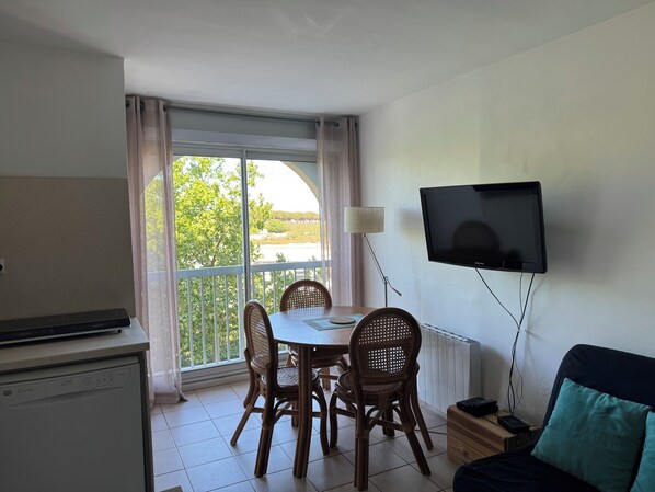 Ein Zimmer mit Esstisch, Stühlen, einem an der Wand befestigten Fernseher, einem Sofa und einem Fenster mit Vorhängen.