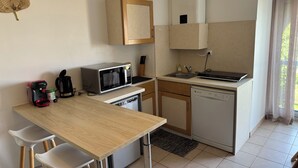 Een compacte keuken met een magnetron, koffiezetapparaat en vaatwasser. Er is een klein eethoekje met een tafel en stoelen.