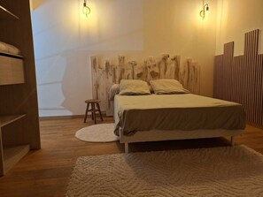 Um quarto com cama, um tapete redondo branco, um banquinho de madeira e uma parede com ripas de madeira verticais.