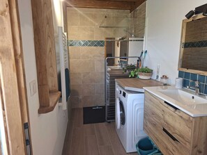 Cozinha compacta com máquina de lavar, pia e área de chuveiro.