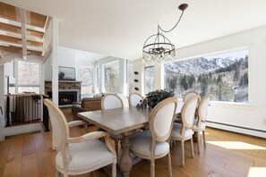 Ein Esszimmer mit Holztisch und -stühlen, einer Chandelüster, einem Kamin und einem großen Fenster mit Bergblick.
