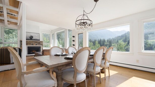 A dining room with a wooden table and chairs, a chandelier, and large windows with a mountain view. - Luxury East Vail Estate w/ Mtn Views & Hot Tub (Vail)