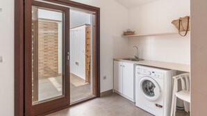 A compact kitchen with a built-in washing machine, a sink, and a small shelf. - Modern Villa for 9 Guests on the Cliffs of Cala Morell, Menorca (Ciutadella)