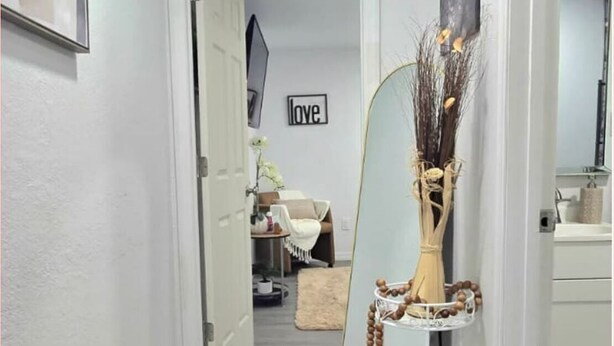 A hallway with a mirror reflecting a room, a 'love' sign on the wall, and a vase with branches. - #33 Private in law suite near USF (Tampa)