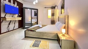 Een moderne hotelkamer met een groot bed, een aan de muur bevestigde televisie, een nachtkastje met een lamp en een badkamer die door een open deur zichtbaar is.
