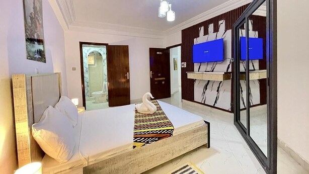 Een hotelkamer met een bed, een televisie, een spiegel en een deur die leidt naar een andere kamer.