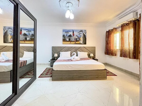 A modern hotel room with a large bed, a mirror, artwork on the walls, and a view of the outside.