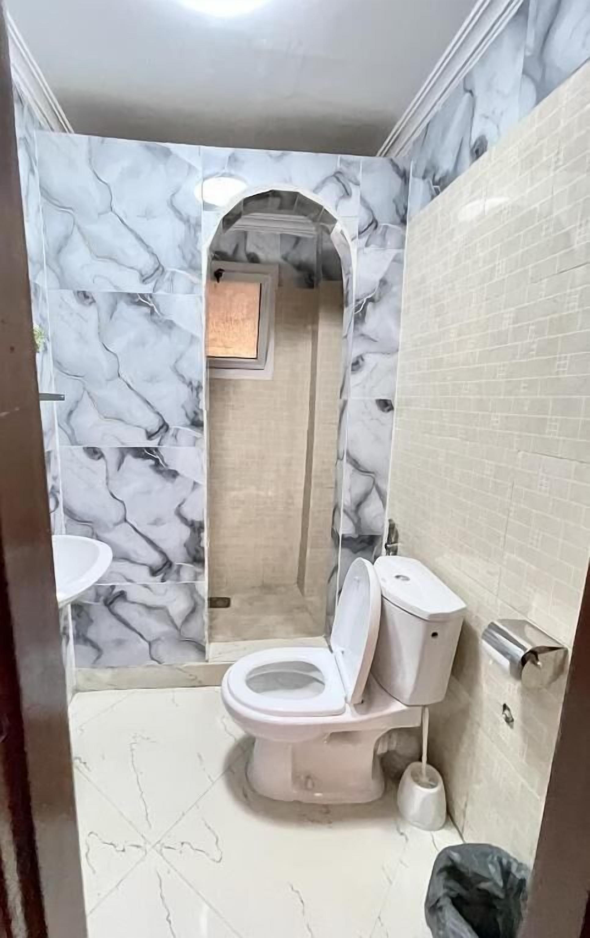 A bathroom with marble-patterned walls, a toilet, a sink, and a shower area.