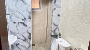 A bathroom with marble-patterned walls, a toilet, a sink, and a shower area.