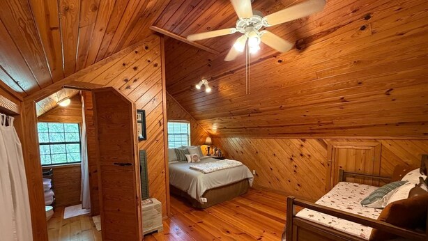 A wooden cabin bedroom with a bed, a ceiling fan, and a window. - Nature Oasis | Hot Tub | Fishing Pond | Fire Pit (Mentone)