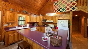 A wooden cabin interior with a kitchen featuring wooden cabinets, a central island, and a ceiling fan. - Nature Oasis | Hot Tub | Fishing Pond | Fire Pit (Mentone)