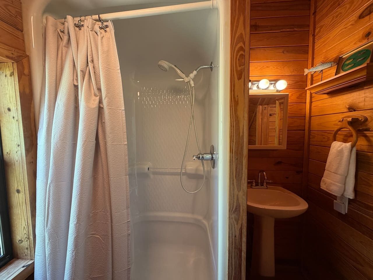 A wooden cabin bathroom with a shower, sink, and towel rack.