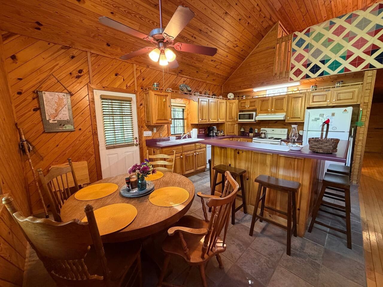 A wooden interior with a dining table, chairs, a kitchen area, and a ceiling fan.