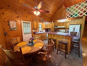 Un interior de madera con una mesa de comedor, sillas, una zona de cocina y un ventilador de techo.