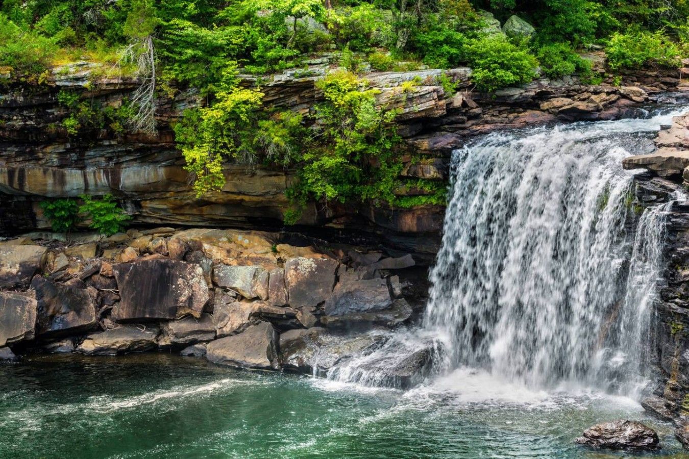 Een waterval stort neer over rotsachtig terrein, omringd door weelderige begroeiing.