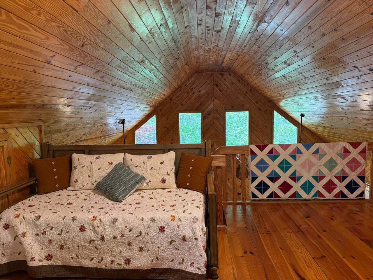 A bedroom with a wooden ceiling, a bed with floral bedding, and a colorful quilt.