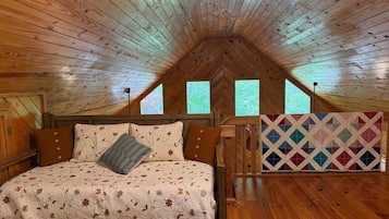 A bedroom with a wooden ceiling, a bed with floral bedding, and a colorful quilt.