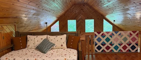 A bedroom with a wooden ceiling, a bed with floral bedding, and a colorful quilt.
