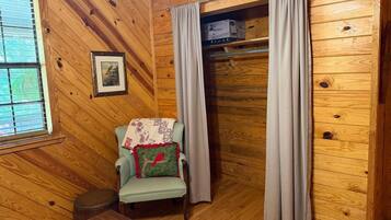 A wooden-paneled room with a chair, a small table, a window with blinds, and a door with curtains.