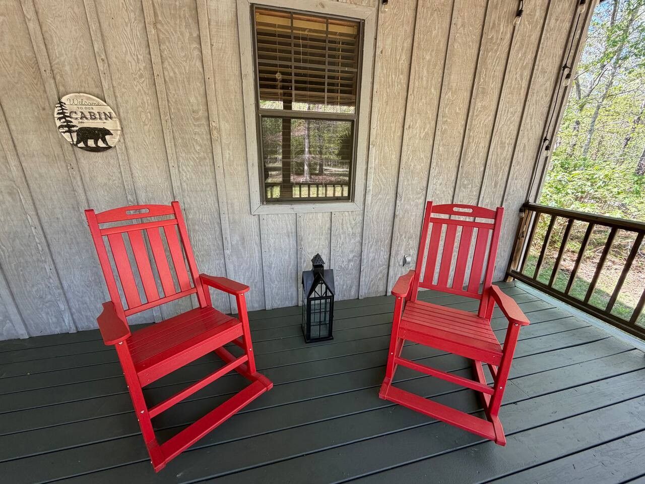 A wooden porch with two red chairs and a lantern.