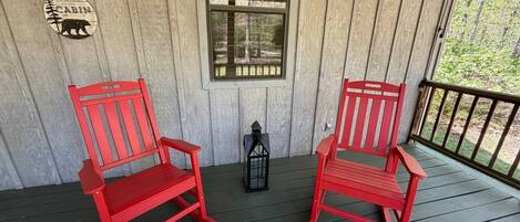 A wooden porch with two red chairs and a lantern.