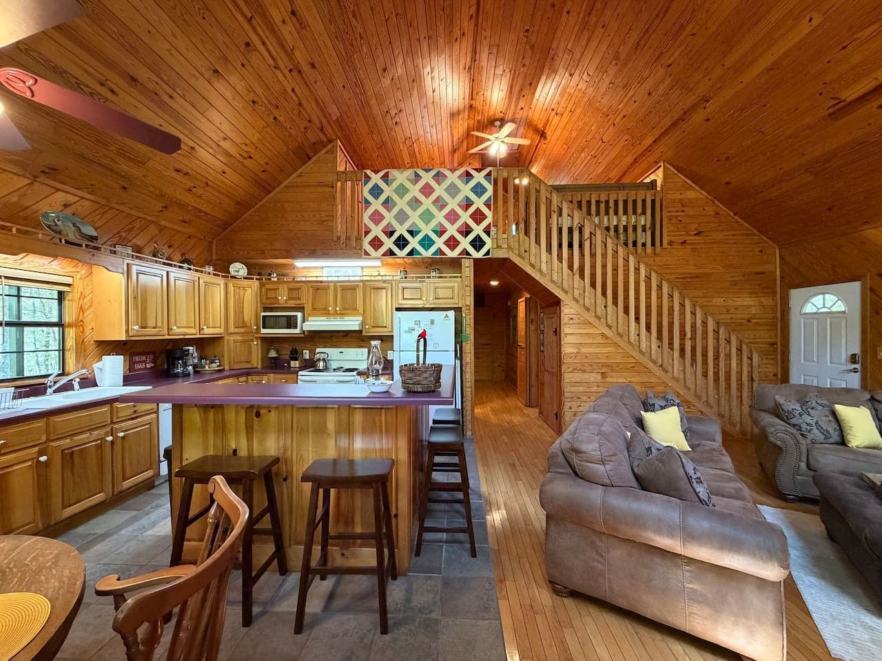 A cabin interior with a kitchen, dining area, and a staircase leading to a loft bedroom.