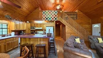 A cabin interior with a kitchen, dining area, and a staircase leading to a loft bedroom.