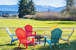 Un espace extérieur verdoyant, avec un foyer et des fauteuils Adirondack aux couleurs vives.