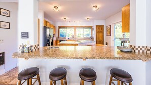 Une cuisine dotée d’un îlot central, de tabourets de bar, de meubles en bois et offrant une vue sur l’extérieur.