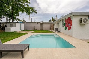 A rectangular swimming pool with a tiled deck, a lounge chair, and a mural of a red flower on the wall. - House with Private Pool & Bar (Fajardo)