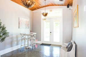 Un interior moderno con techo de madera, un comedor con mesa y sillas, una puerta con letrero de salida y una planta en maceta.