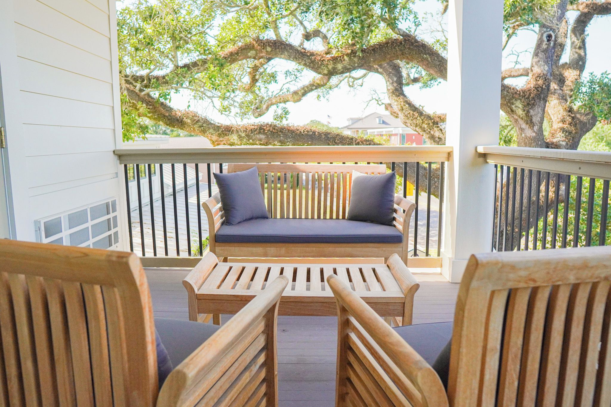 Une terrasse en bois avec un banc et deux chaises, donnant sur un grand arbre.