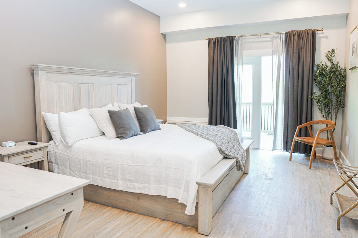 Une chambre à coucher comprenant un lit, une table de chevet, une chaise et donnant sur l’extérieur.