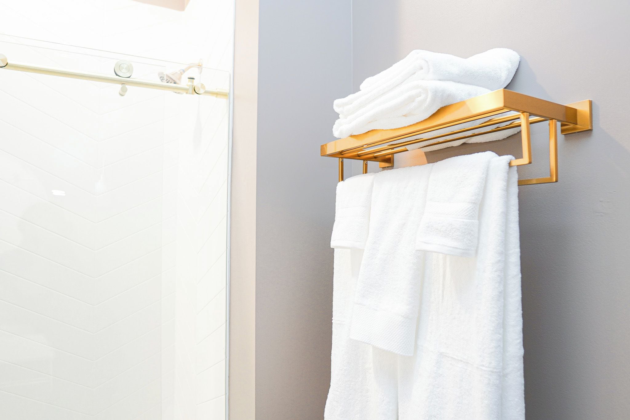 A bathroom with a glass shower door, a towel rack with folded towels, and a towel on a wall.