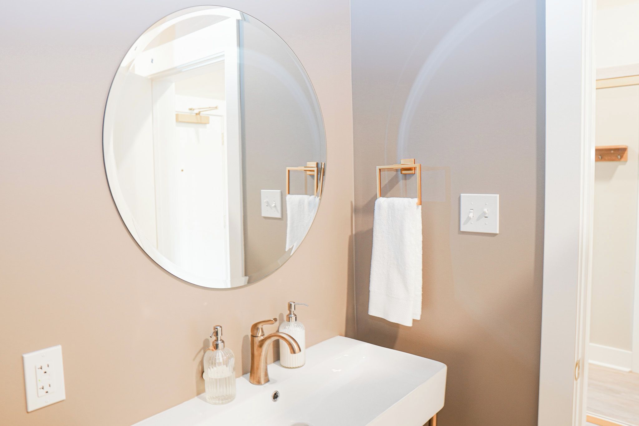 Une salle de bain avec un miroir rond, un lavabo blanc, un porte-serviettes et un présentoir à serviettes en bois.