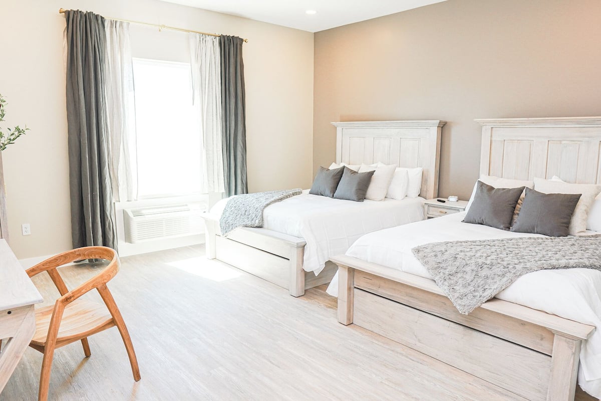Une chambre avec deux lits, une chaise en bois, une table de chevet et une fenêtre avec des rideaux.