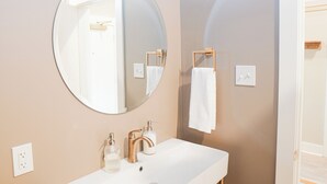 A bathroom with a round mirror, a white sink, a towel rack, and a wooden towel holder. - Hotel Whiskey in Long Beach (Long Beach)