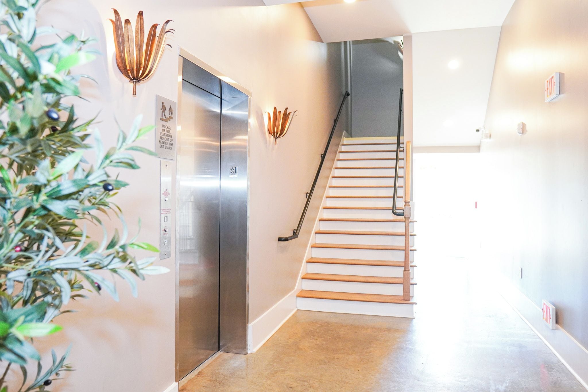 A modern interior with a staircase, a wall-mounted light fixture, and an elevator.